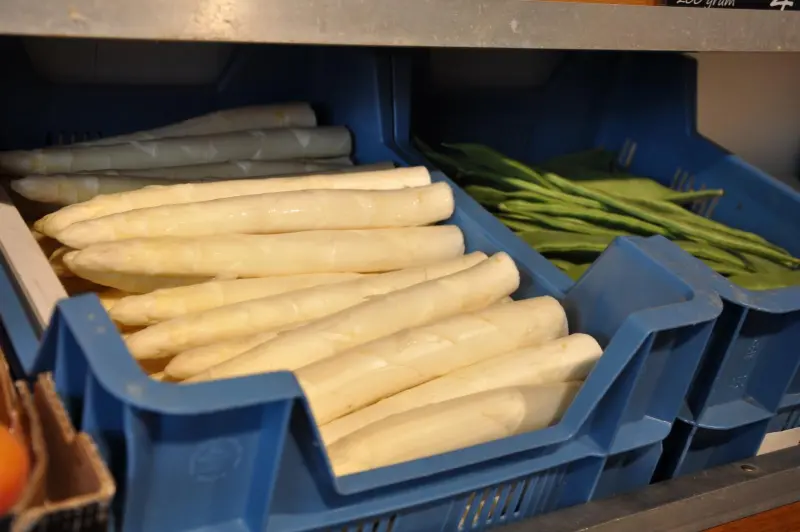 Een krat met witte asperges naast een krat sperziebonen
