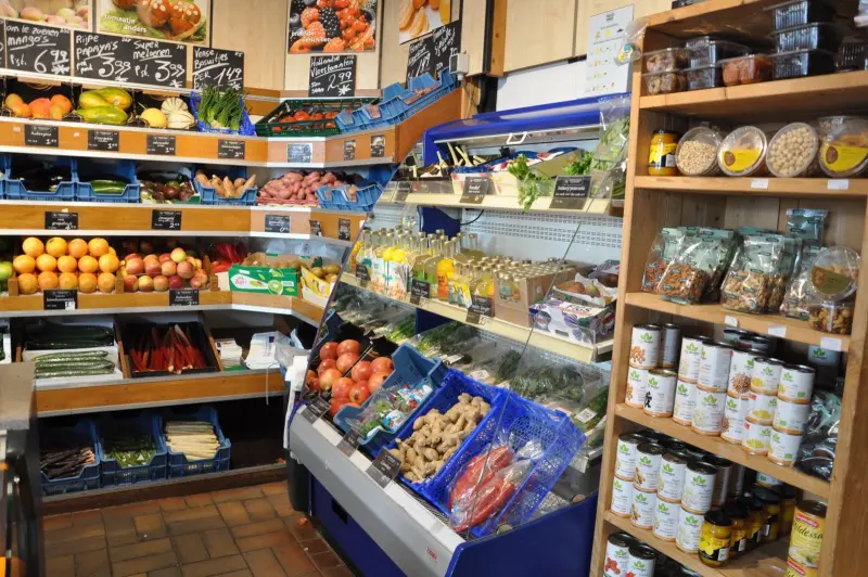 Hoek van de winkel met schappen fruit, een koeling en een kast met potten en noten
